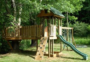 Frot with catwalk bridge to the tree deck, a rope pull-up climber wall, slide, and attached swing beam - Asheville Playgrounds