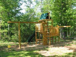 Multiple level play set with swings, trapeze, disc swing, rock wall, and slide... with a bench table underneath - Asheville Playgrounds